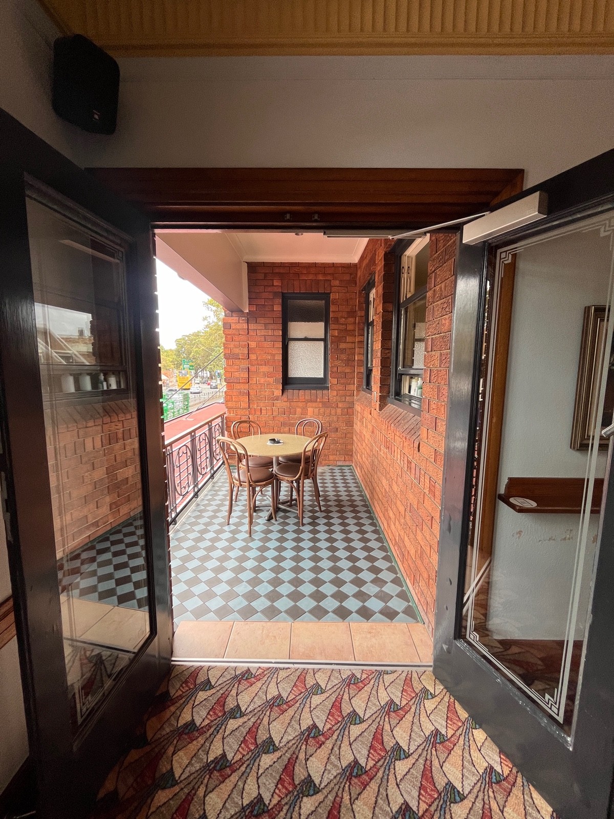 From after large table facing straight. Glass double doors with dark brown frame. Pull silver handles from middle. Table and chairs directly ahead.