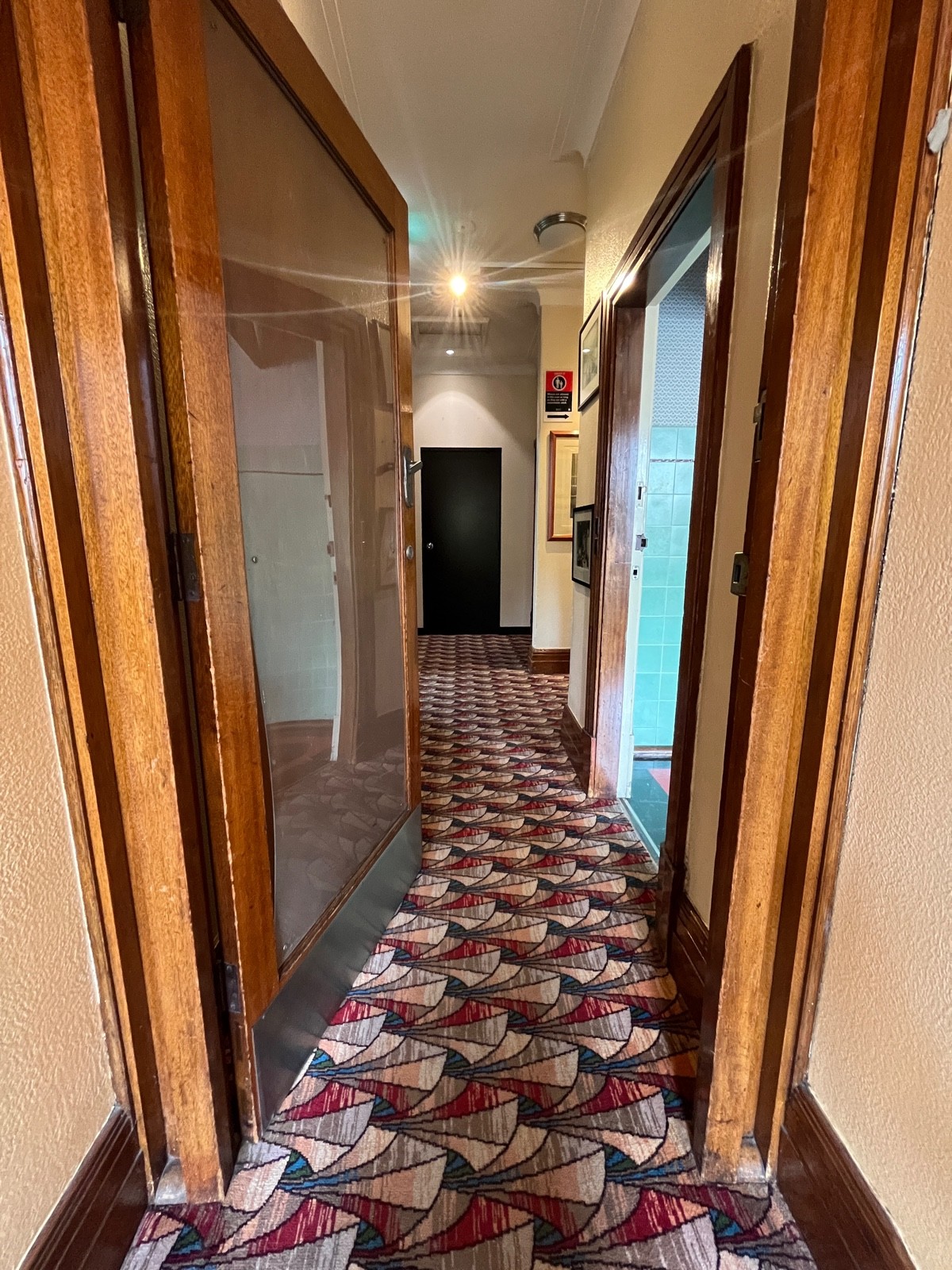 From top of stairs facing straight. Glass door with brown wooden frame. Push from right.