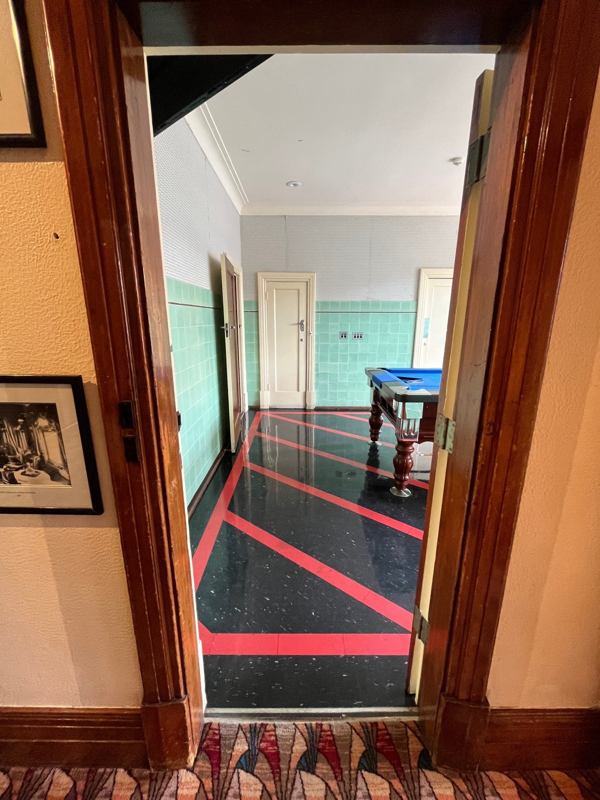 From glass door facing right. Brown wooden door ahead. Turn gold handle and push from left.