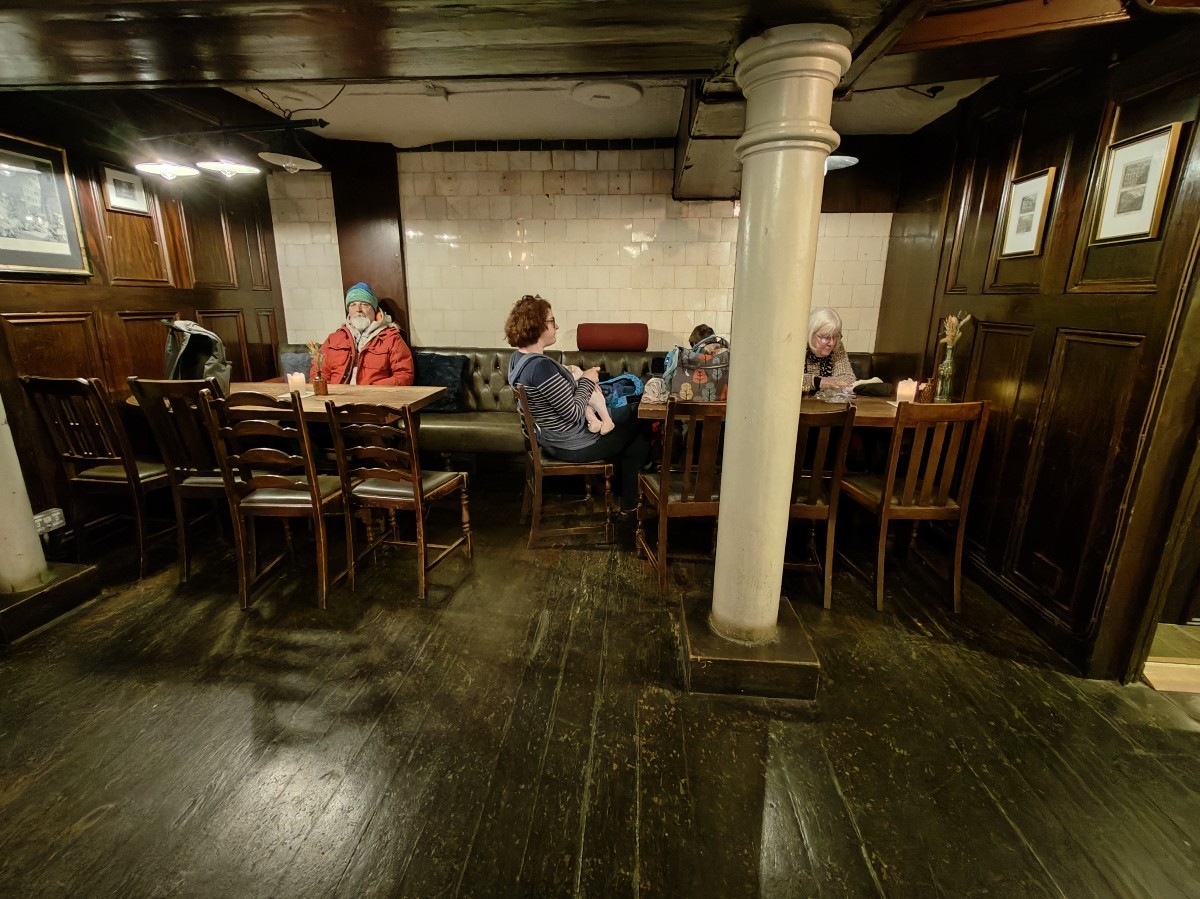 From top of stairs facing straight. Half booth along back wall. White pillar at back right.