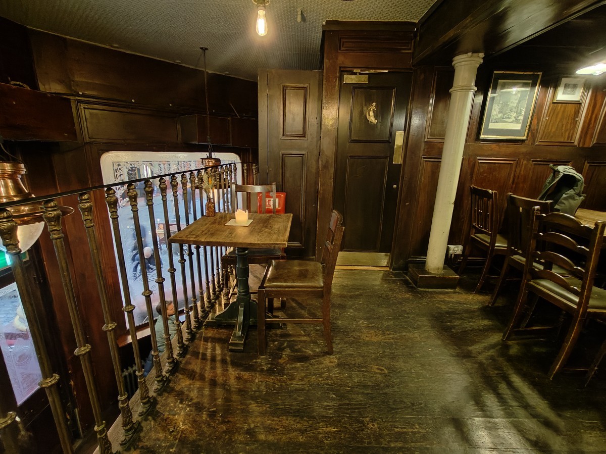 From top of stairs facing left. Table and chairs on left. Path ahead to female toilet. Pillar on right.