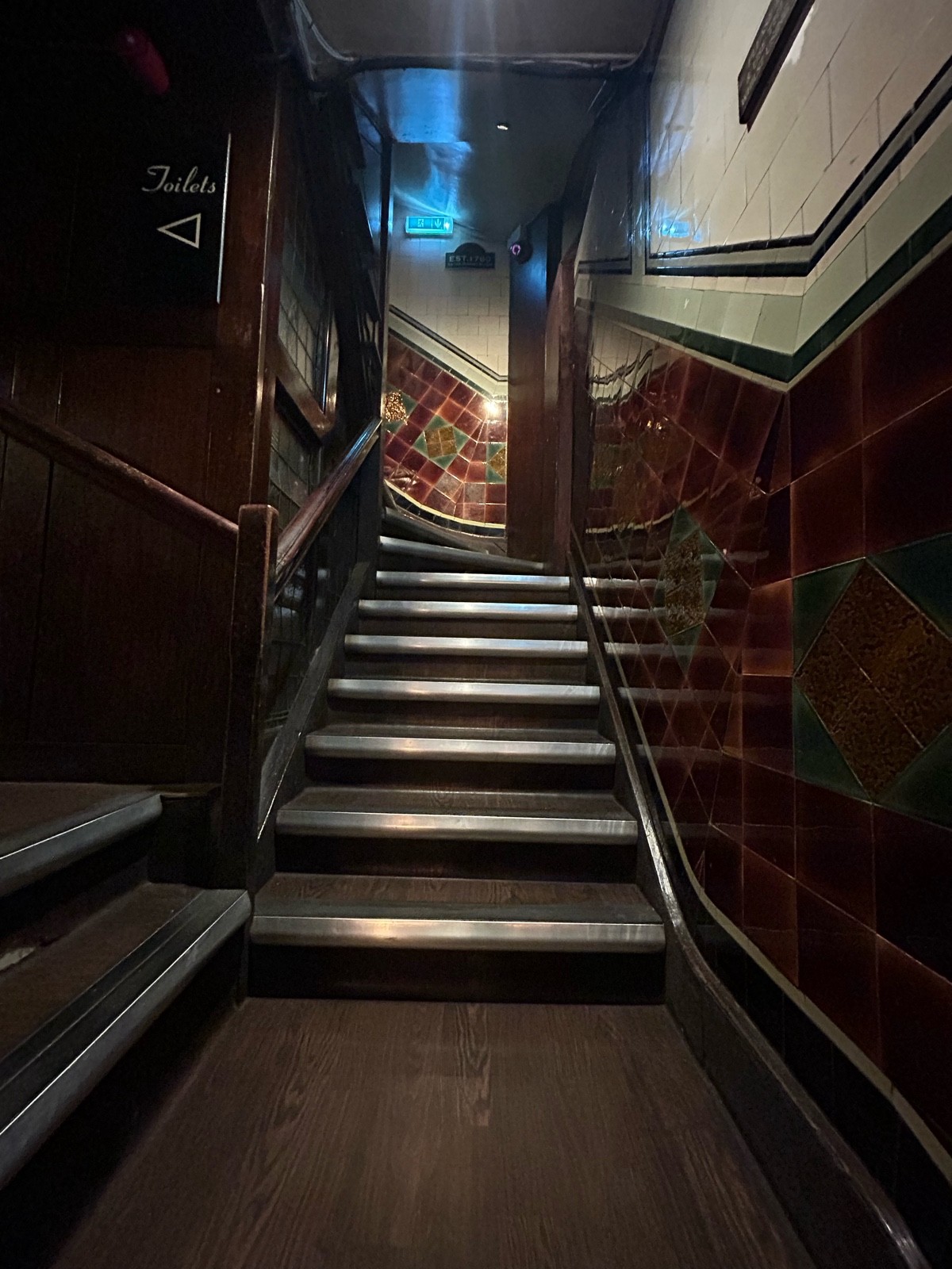 From top of first flight facing straight. Steps on left to upstairs area. Second flight of stairs ahead curve left. Handrail on left.