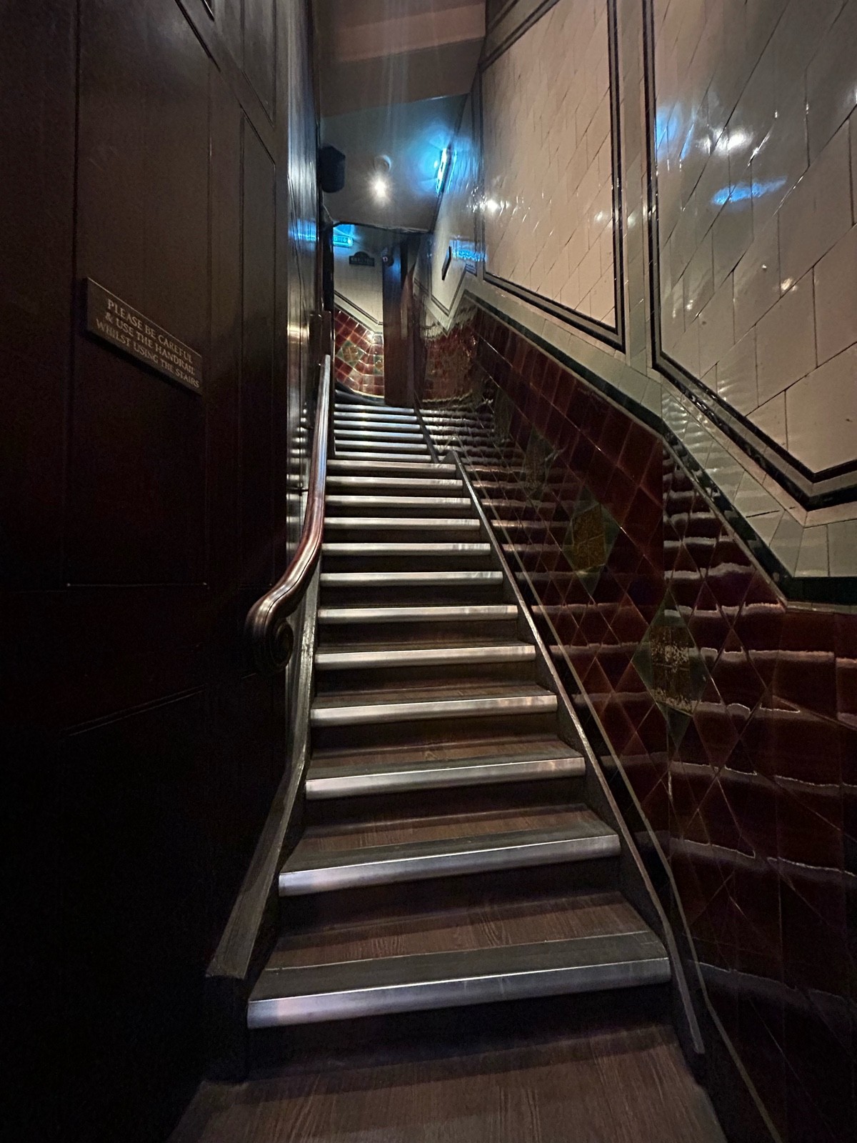 From archway facing straight. Flight of stairs ahead. Wooden handrail on left.