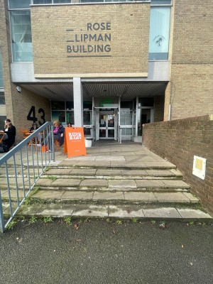 From street facing venue. Steps going up ahead. Grey metal handrail to left. Steps up to its left as well.