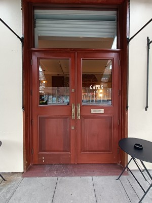 Glass door with brown wooden frame. Push golden, handles in middle to open.