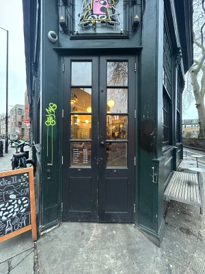 Glass doors with black frame ahead. Pull black handle in centre to open. A-frame sign on left.