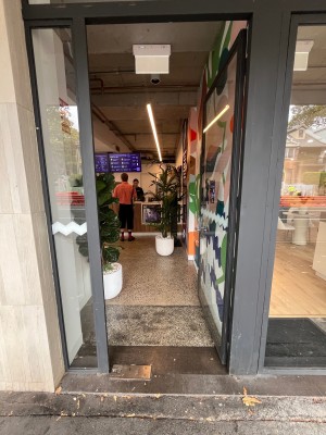 Grey metal-framed glass door. Push from silver handle on left to open.