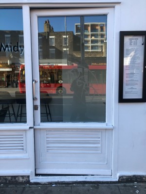 Glass door with white frame. Push handle on left to open.