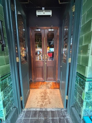 Glass door with green wooden frame ahead. Push metal plates at center to open leading to second door.