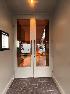 Glass doors with grey wooden frame ahead. Pull metal handles at center right of left door to open.