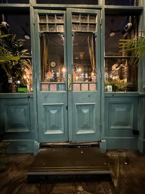 Blue wooden doors with glass panels ahead. Pull gold handle in centre to open.