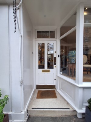 From pavement facing venue. One step up to doormat and door behind. White door with glass panel. Push on right to open.
