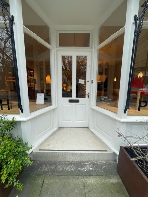 White wood-panelled glass door. Push from brass handle on right to open. Step up before door.
