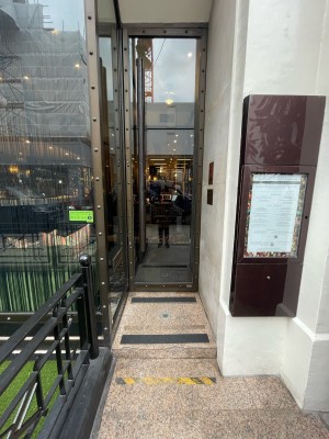 From street facing venue. Glass door with metal frame ahead. Push or pull black metal handle on left to open. Step up before door.