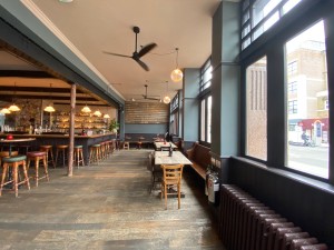 From entrance facing right. Half booth with tables and chairs along right and back wall. Bar counter with stools ahead to back left.