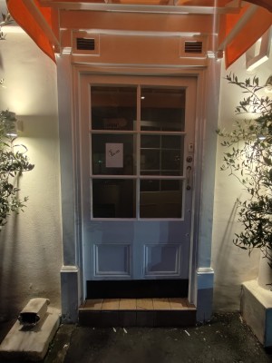 White framed preceding glass door. Push golden handle on right to open. Doorbell above handle.