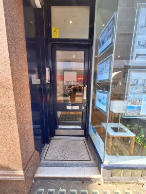 One step up to glass door with blue frames. Push on right to open.