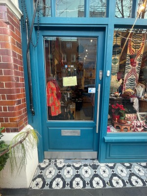 Glass door with blue frame ahead. Silver metal handle on right. Push doorbell on right of door for staff to open. Door opens inwards from right.