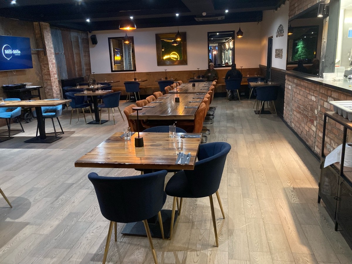 From end of path facing straight. Open kitchen along right. Tables and chairs ahead along center and along back and left.