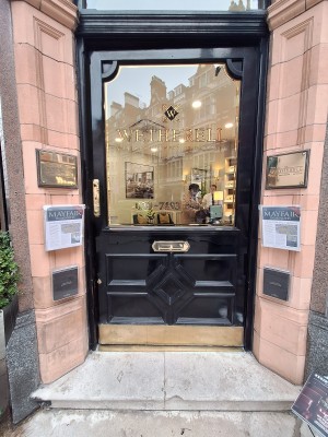 Black door with glass panel ahead. Push brass handle on left to open. Doormat after door.