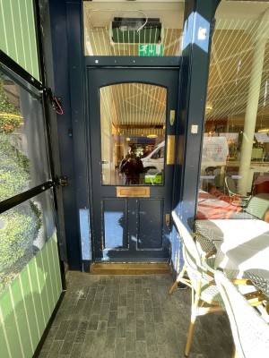 Green wood-framed glass door ahead. Doorbell on left. Push from brass plate on right to open.