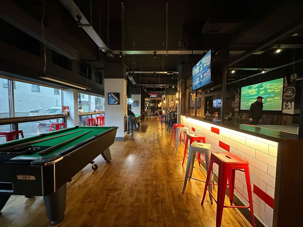 From bottom of step facing straight. Pool table to left. White pillar behind. High table and stools along right.