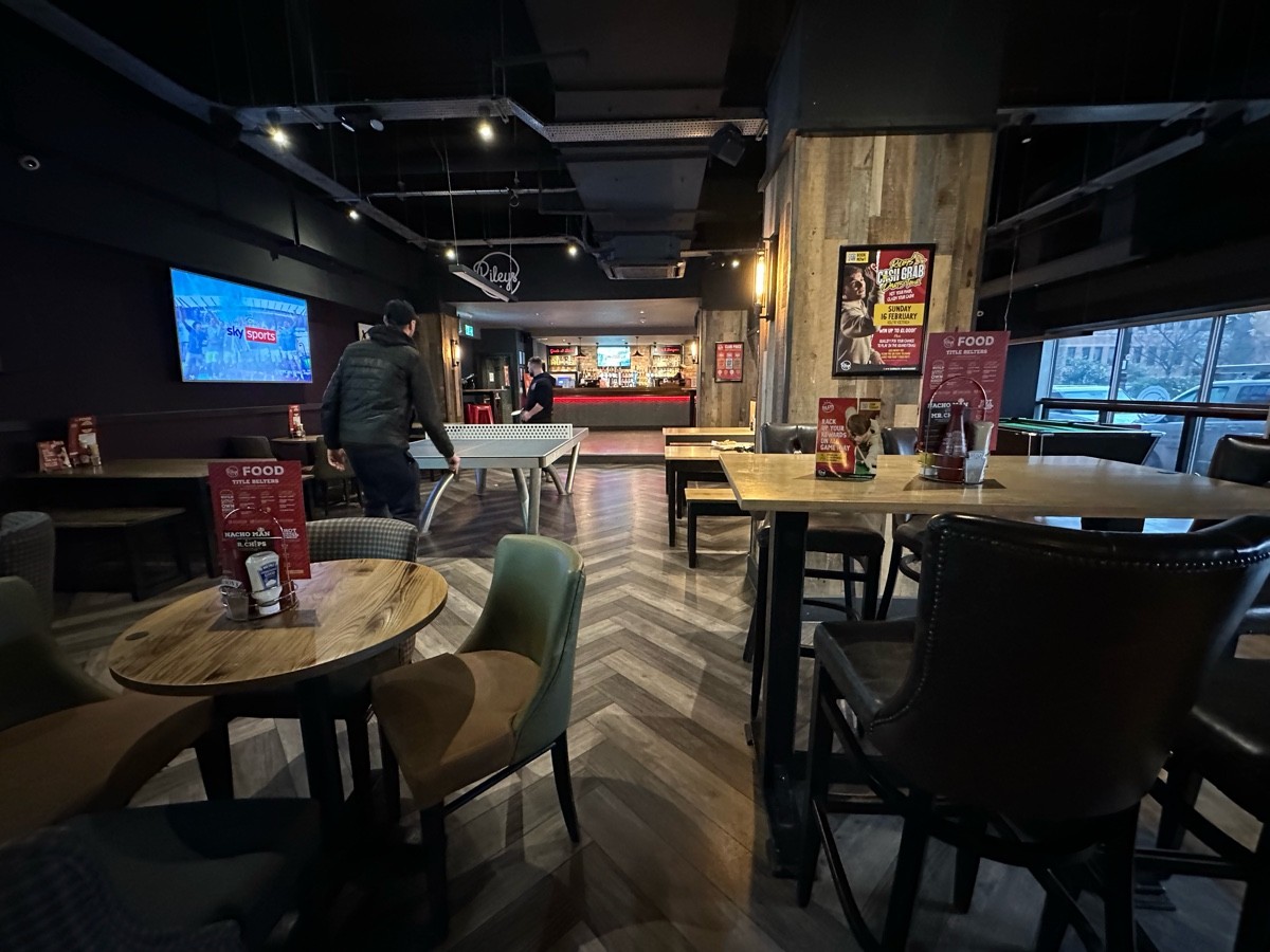 From after high table facing right. High tables and stools to right. Tables and benches behind. Tables and chairs to left. Ping pong table behind.