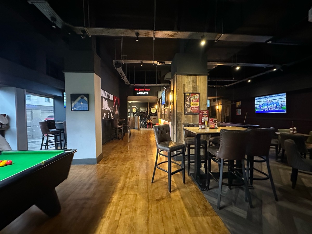 From white pillar facing straight. Pool table to left. 2nd pillar behind. High tables and stools to right.
