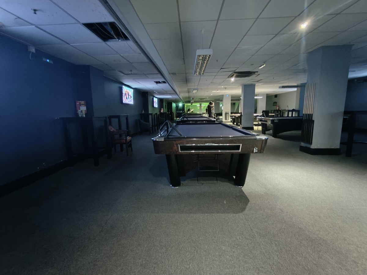 From bottom of steps facing straight. Pool tables along centre and right. Stools along left wall. Columns on right obstructing path.