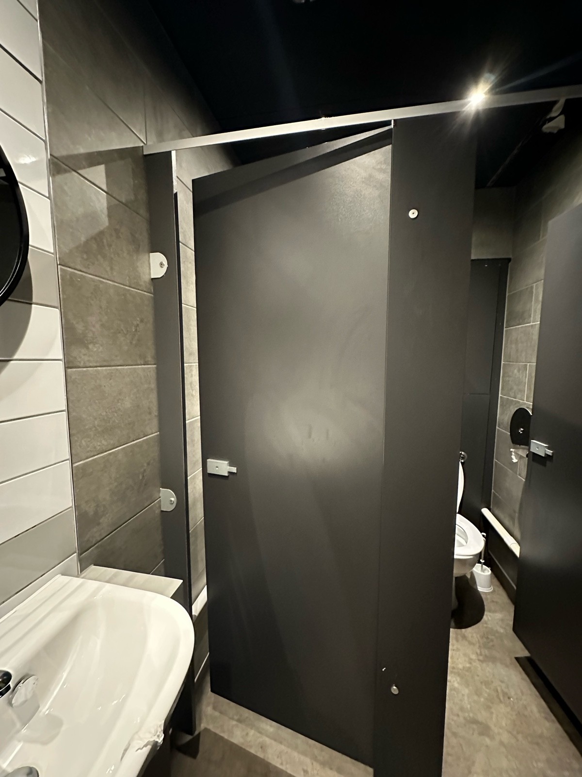 From end of sinks facing straight. Black wooden cubicle door ahead. Push from left to open.
