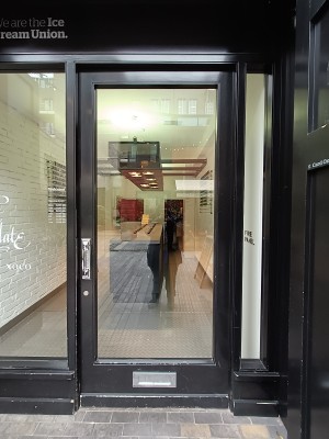 Glass door with black, metal frame. Push silver handle on left to open.