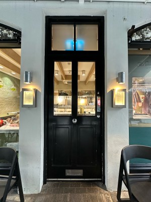 Black and glass panelled door. Push from right to open. Tables and chairs to left and right.