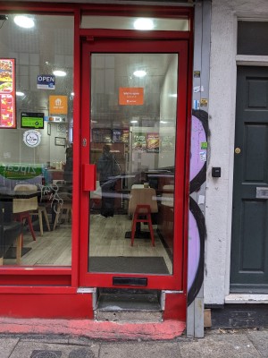 Glass door with red frame and red handle on left. Push to open.