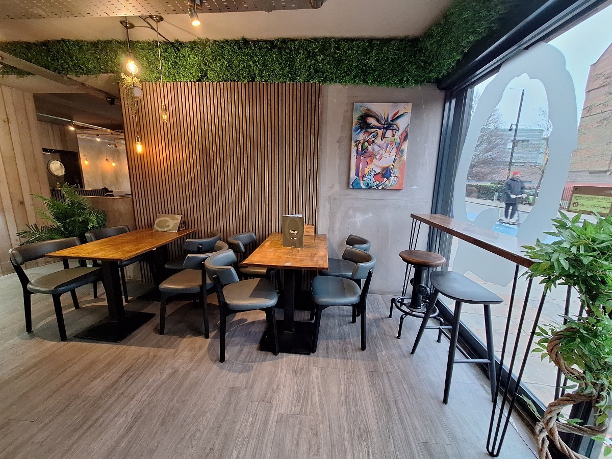 From entrance facing right. High table and stools on right. Tables and chairs along back.