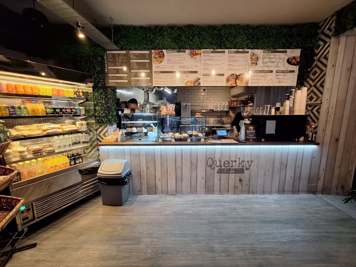 From before counter facing straight. Fridge on left. Till counter behind. Path on right to back area.