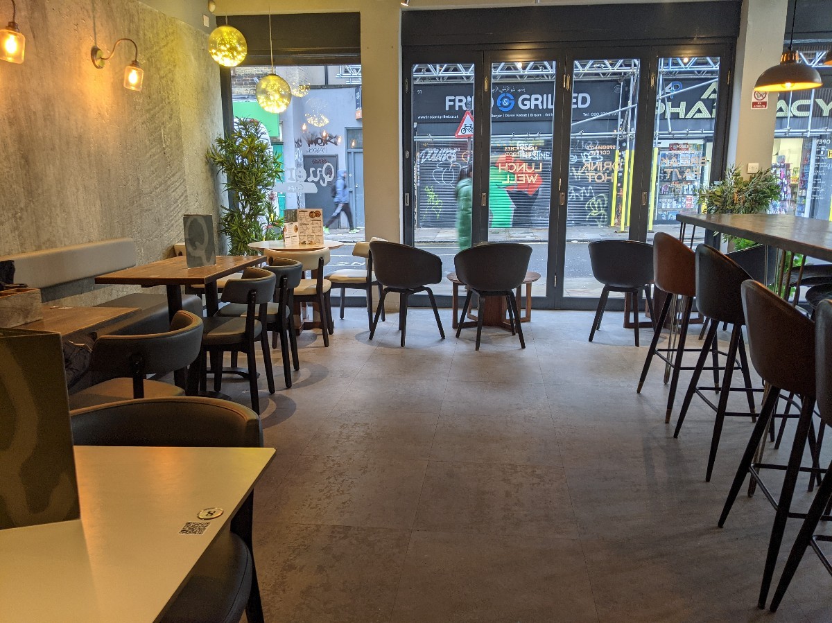 From toilet door facing right. Half booths along left, high tables with stools along right. Chairs and low tables at back.