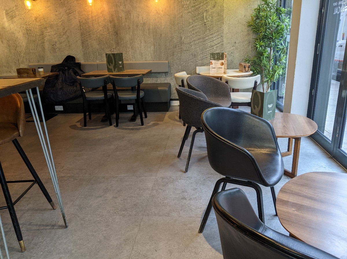 From alternative entrance facing left. High tables with stools on left, half booths at back. Low tables with chairs on right.