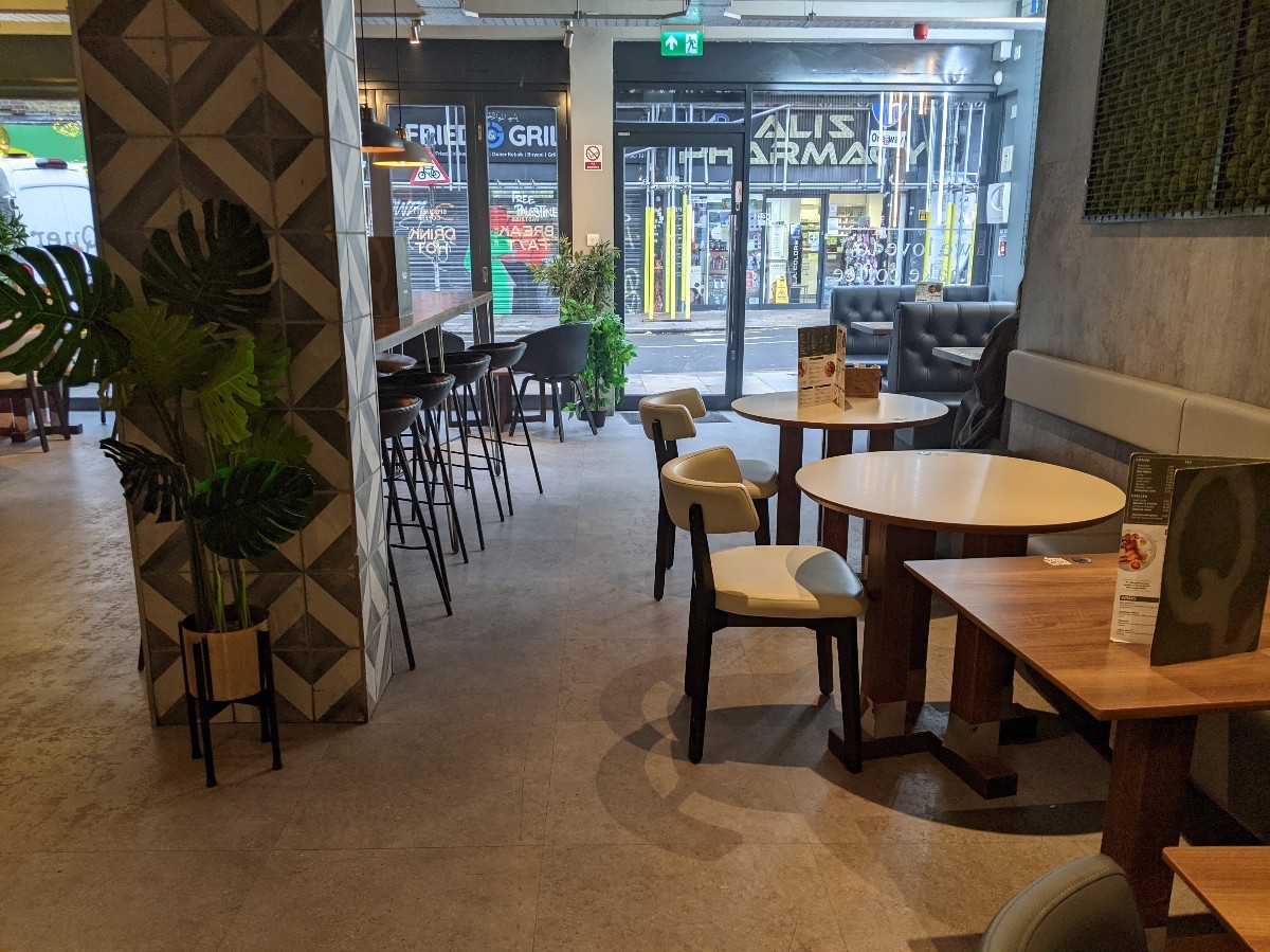 From end of ramp facing straight. Pillar left, high tables with stools behind. Half booths along right, booths behind. Alternative entrance at back.