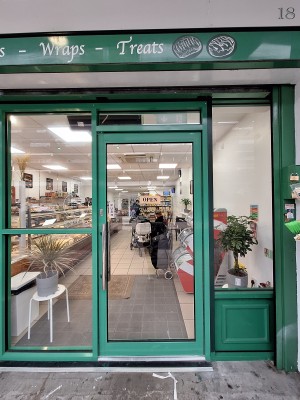 Glass door with green frames. Push metal handle on left to open.