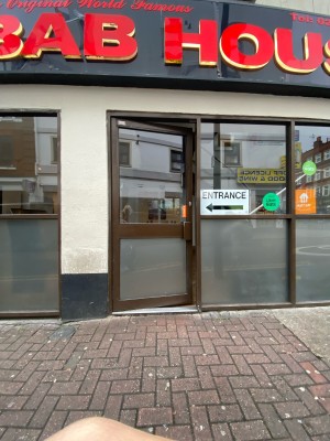 Glass door with brown frame ahead. Push brown metal handle on right to open.