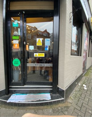 3 steps up to entrance. Glass door with black frame ahead. Push from metal handle on left.