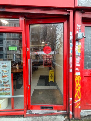 1 step up to entrance. Glass door with red frame ahead. Pull from handle on left to open.