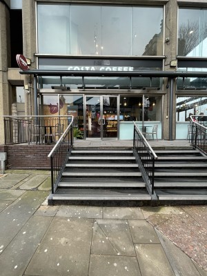 From street facing venue. Stairs ahead, leading up. Metal handrails along left and right.