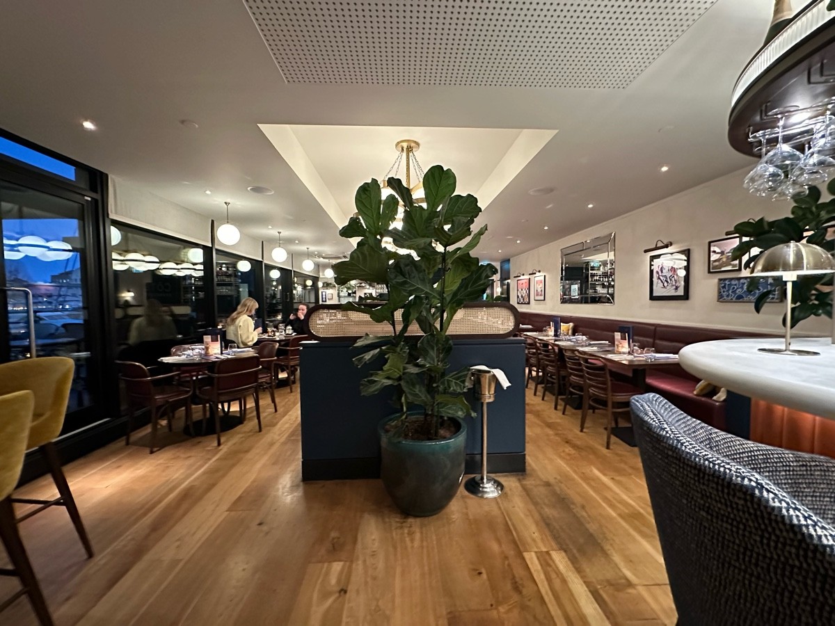 From corner of bar facing straight. High table and stools to left. Divider and plant ahead. Half booths to back right.