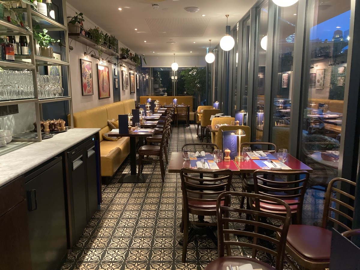 From curtains facing straight. Staff desk along left. Half booths tables and chairs behind and on back. Tables and chairs along right.