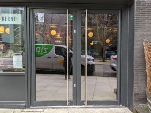 Glass doors with grey frame and metal handles in centre. Push to open.