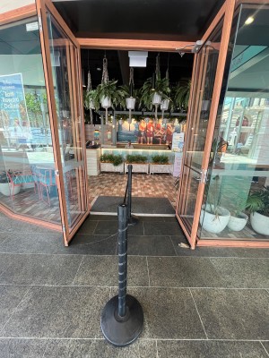 Glass double doors with brown wood frame and silver handle on right door. Pull from middle. Queue divider in middle of path through door.