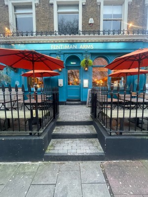 From street facing venue. Opening ahead with black metal bannisters along both sides. Three steps up at foot of opening.