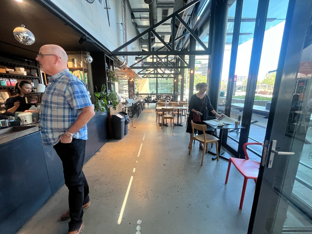 From counter facing right. Counter on left followed by bins. Tables and chairs on right wall ahead.