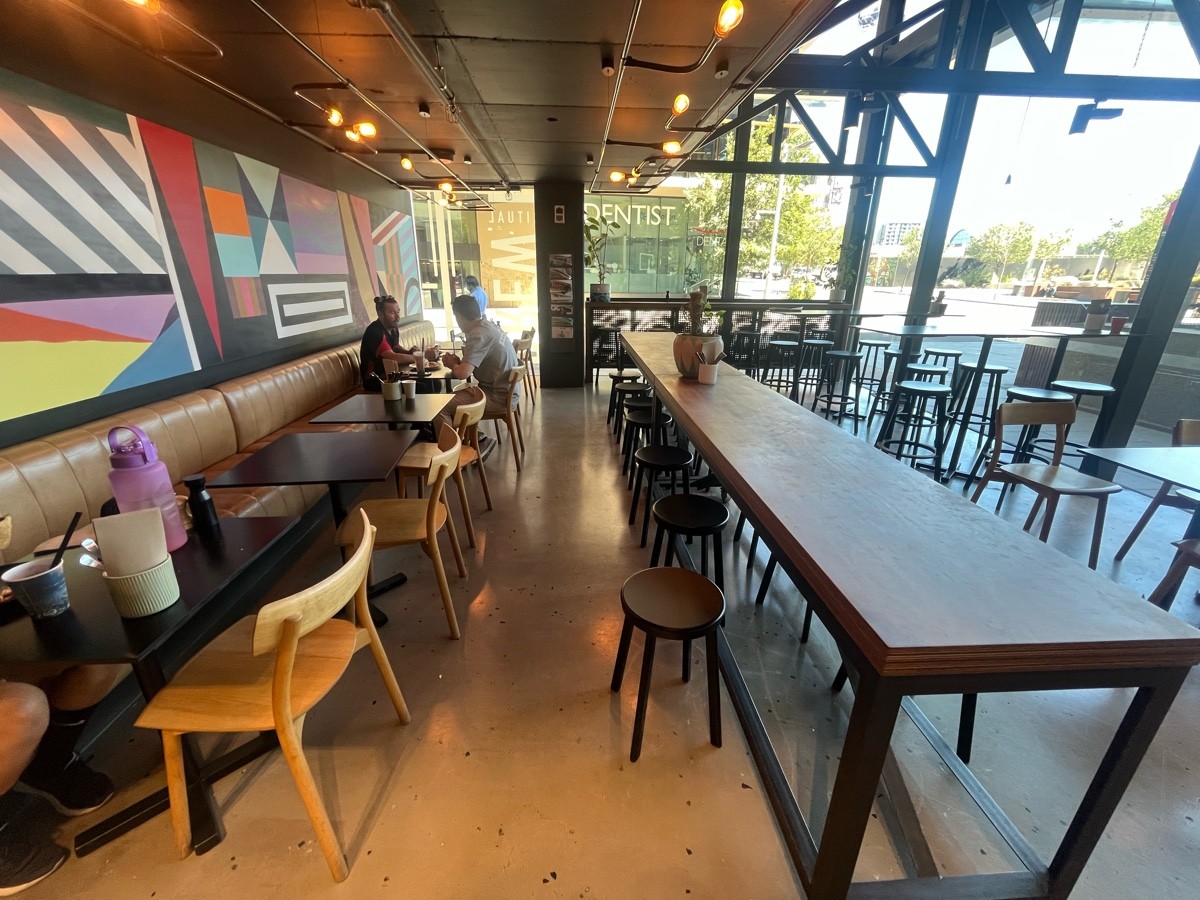 From before bathroom door facing right. Half booths along left wall. Table and backless stools along right.